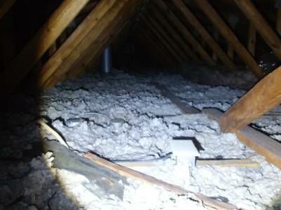 Grey blown-in insulation lying level with the ceiling joists in a dim truss attic