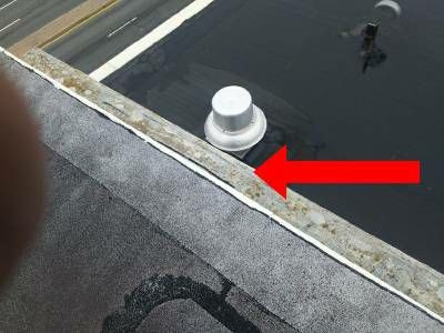 The edge of a flat roof ledge with its top surface worn away to bare wood, a red arrow pointing along it