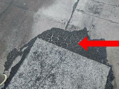 A grey patch on a flat roof membrane, its edge cracked into a crazed black pattern, with a red arrow pointing to it
