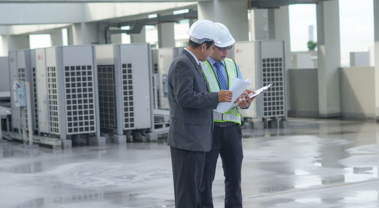 Two inspectors reviewing notes beside rooftop HVAC units on a commercial building
