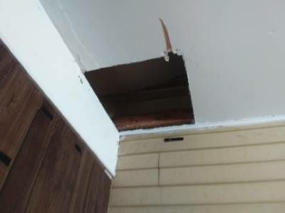 A rectangular hole cut into a white garage ceiling where it meets a wood-panelled wall