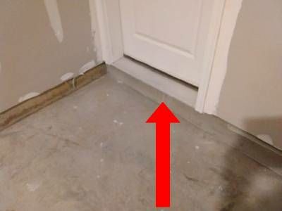 The base of a white fire door in a garage, with a red arrow pointing to the empty gap under its threshold