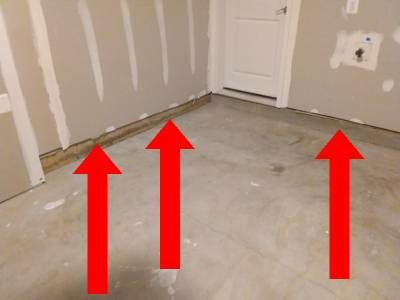 Bare garage drywall with three red arrows pointing to green foam insulation showing beneath the bottom edge of the wall