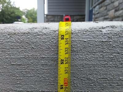 A yellow tape measure held vertically against the side of a concrete porch, reading past 50 inches