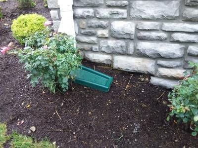 A mulched flower bed beside a stone veneer porch wall, with the grey foundation visible below the stone