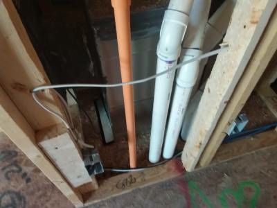 Orange and white vent pipes rising through an open floor penetration between wall studs, with no fireblocking around them