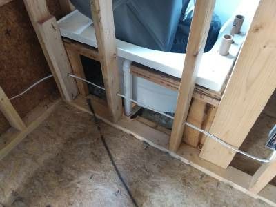 A white bathtub set into open framing, with wiring and pipes running through the bays beneath it