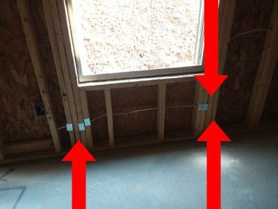 Open basement framing beneath a window, with red arrows pointing to wires passing through the studs