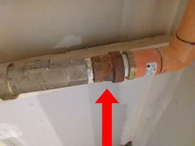 A brass coupling on an orange sprinkler pipe near a ceiling, heavily rusted, with a red arrow pointing up at it