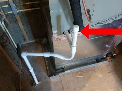 White PVC condensate drain lines at the base of an air handler, with a red arrow pointing to the capped clean-out on the line