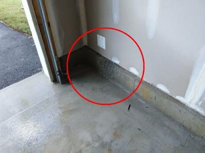 A garage corner beside an open door, with a red circle around a broken-out section of the concrete foundation at the base of the wall
